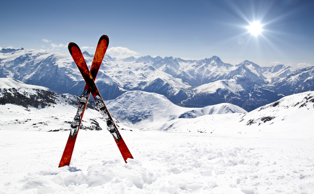 Paire de skis plantee dans la neige devant un panorama de montagnes